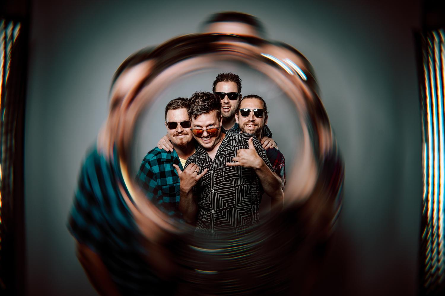 The four members of The Wild Blue in sunglasses, framed by a swirl of light